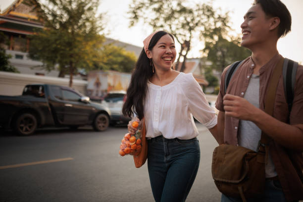 A smiling couple holds a bag of oranges as they walk through the city.